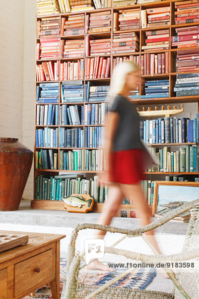 Blurred view of woman walking by bookcase