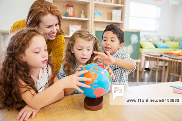 Students and teacher examining globe in classroom