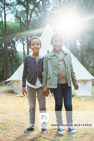 Girls smiling by teepee at campsite