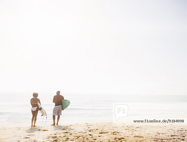 Couple carrying surfboards on beach