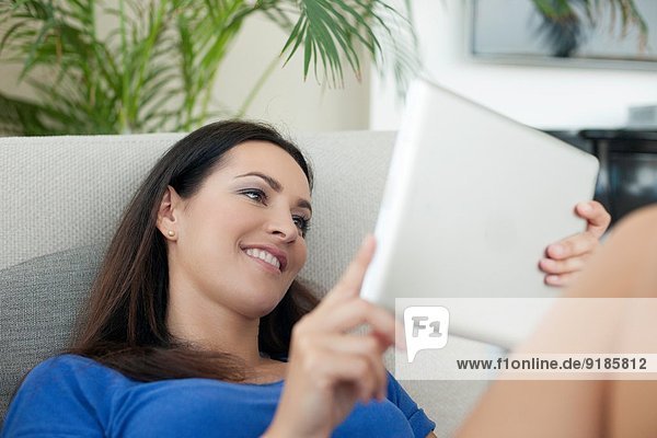 Young woman reclining on sofa using digital tablet