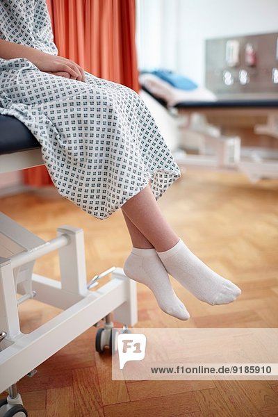 Mädchen im Krankenhausbett sitzend  im Untersuchungskittel