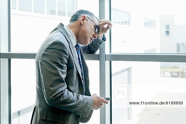 Businessman with smartphone leaning on glass wall