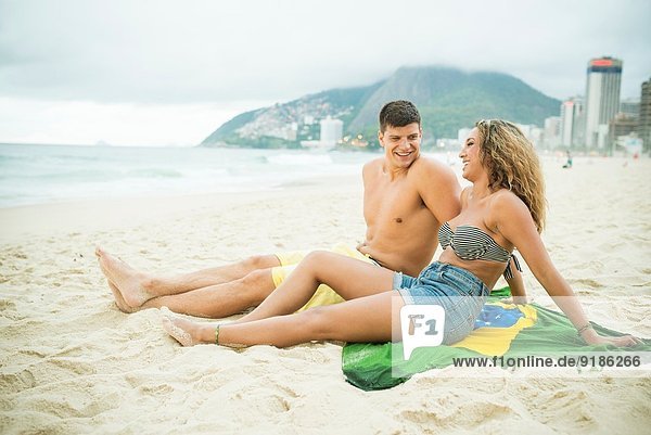 Young couple sitting on brazilian flag  Ipanema Beach  Rio de Janeiro  Brazil