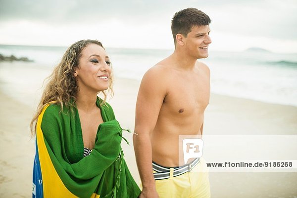 Junges Paar beim Strandspaziergang  Frau in brasilianischer Flagge  Ipanema Beach  Rio de Janeiro  Brasilien