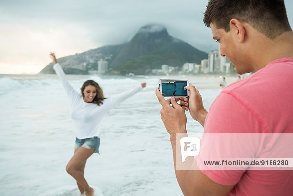 Young couple photographing with smartphone on Ipanema Beach  Rio de Janeiro  Brazil