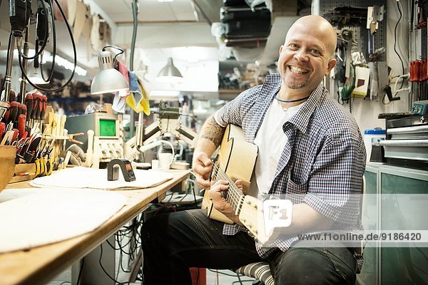 Porträt des Gitarrenbauers beim Stimmen der Akustikgitarre in der Werkstatt