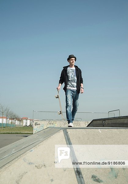 Junger Mann läuft durch den Skatepark und trägt Skateboard.