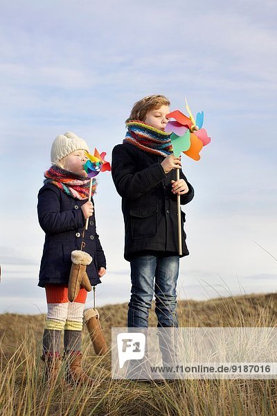 Bruder und Schwester blasen auf Papierwindmühlen an der Küste
