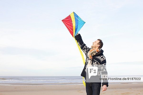 Mid adult man holding up kite on beach,  Bloemendaal aan Zee,  Niederlande