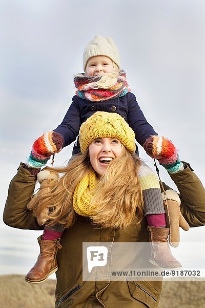 Lächelnde mittlere erwachsene Frau mit Tochter auf den Schultern an der Küste