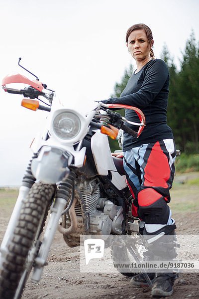 Portrait of young adult female motorcyclist with motorcycle
