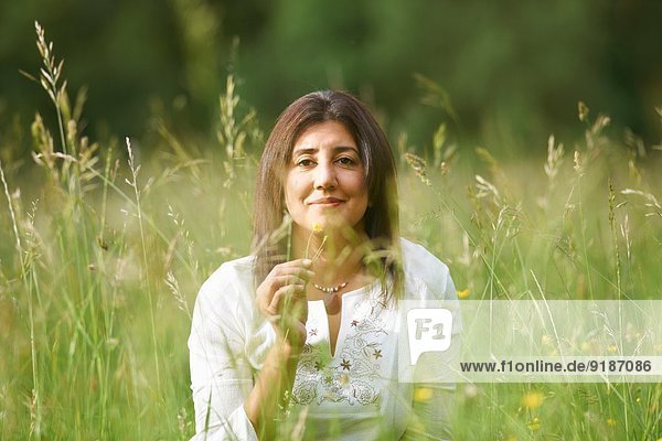 Porträt einer reifen Frau in langem Gras mit Butterblume