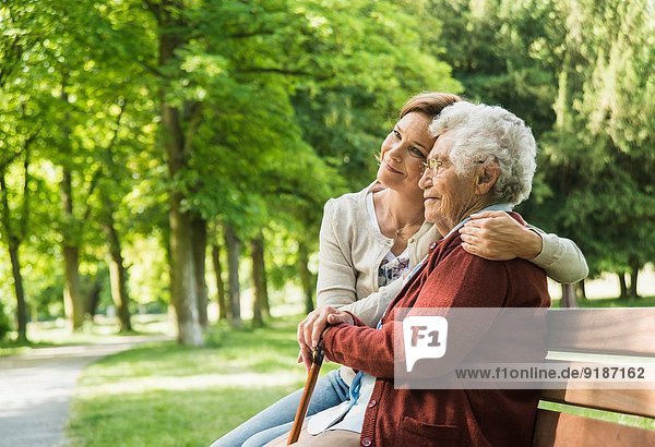 Senior woman sitting on park bench with granddaughter