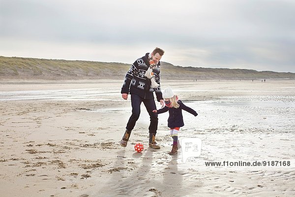 Mid adult man with daughter playing football on beach  Bloemendaal aan Zee  Netherlands