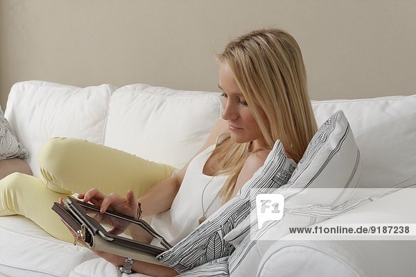 Junge Frau auf Sofa mit Touchscreen auf digitalem Tablett