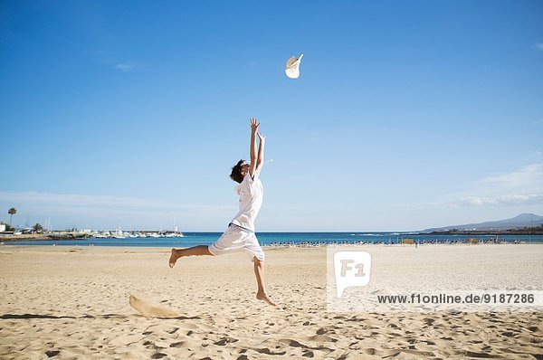 Boy jumping and throwing hat mid air on beach