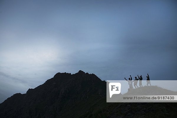 Silhouette von vier jungen erwachsenen Männern mit erhobenen Armen auf dem Gipfel des Berges