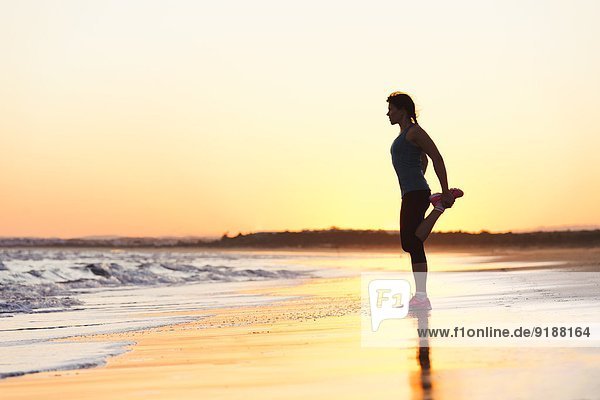 Woman exercising on beach at sunset