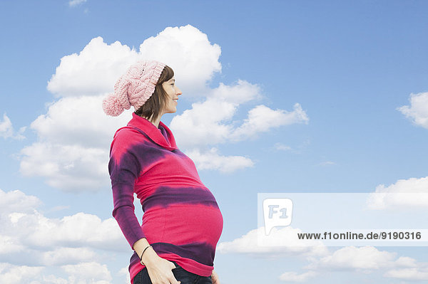 Seitenansicht einer schwangeren Frau  die gegen den bewölkten Himmel steht.