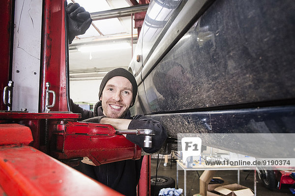 Porträt eines selbstbewussten Kfz-Mechanikers  der sich in der Werkstatt auf das Hebezeug stützt.