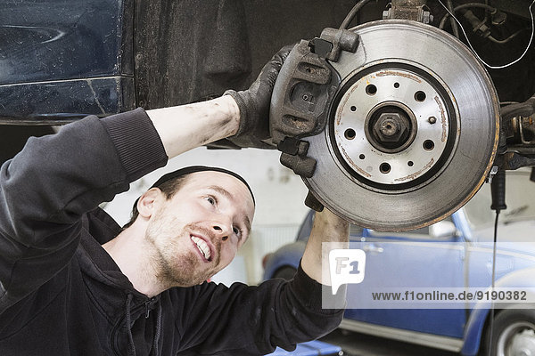Lächelnder Arbeiter repariert Auto in Autowerkstatt