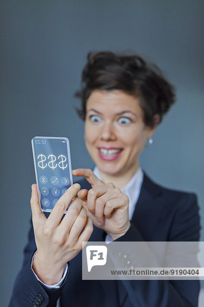 Überraschte Geschäftsfrau mit futuristisch transparentem Handy mit Dollarzeichen