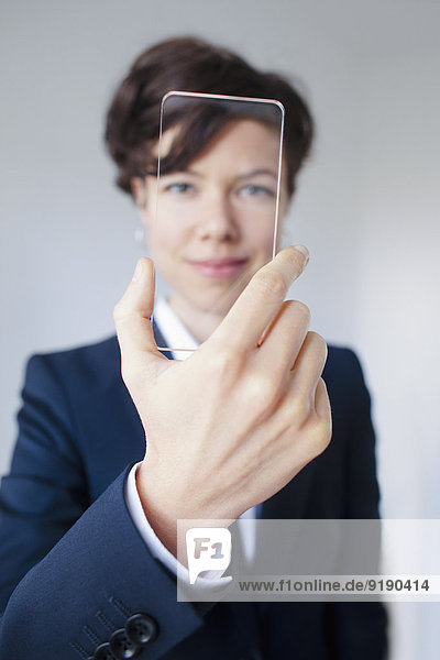 Zuverlässige Geschäftsfrau blickt durch futuristische transparente Smartphone