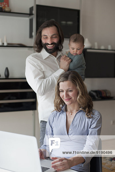 Vater mit Baby Girl schaut Frau mit Laptop zu Hause an