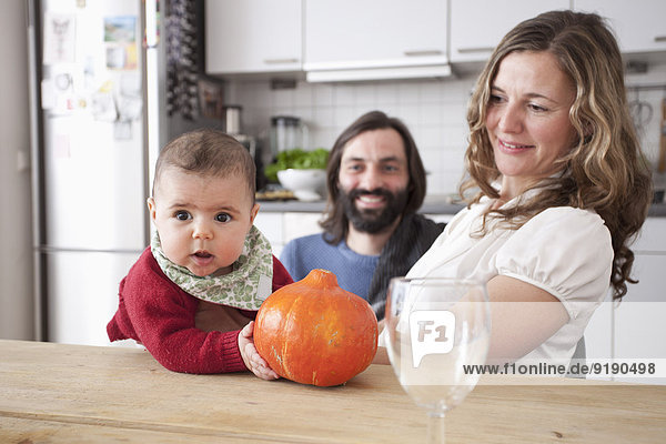 Eltern mit Baby halten Kürbis am Tisch in der Küche