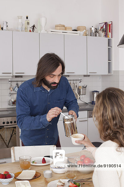 Mann fügt Zucker zum Frauenkaffee am Frühstückstisch hinzu