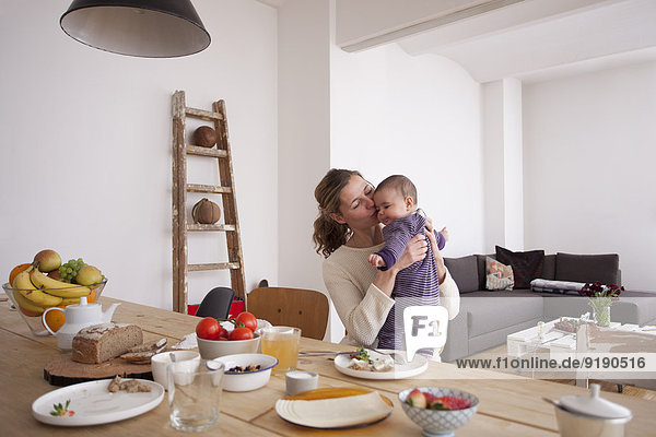 Liebende Mutter küssendes kleines Mädchen am Frühstückstisch