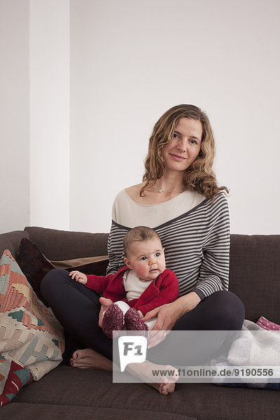 Portrait of mid adult woman sitting with baby girl on sofa at home