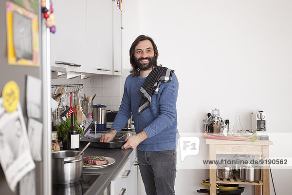 Lächelnder Mann schaut weg beim Zubereiten von Speisen in der heimischen Küche.