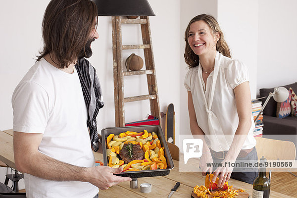 Lächelndes Paar bereitet zu Hause ein Kürbisgericht zu.