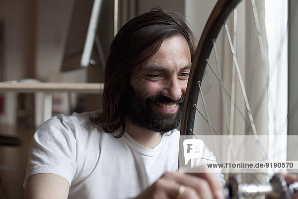Lächelnder erwachsener Mann  der das Fahrrad zu Hause repariert.