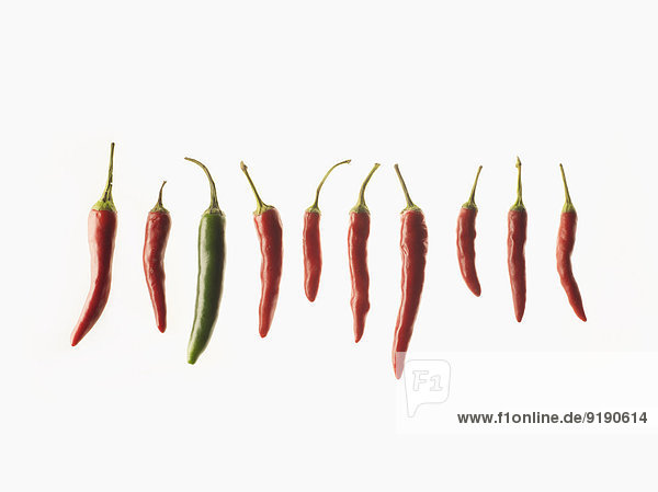 Grüner Chili inmitten roter Chilis auf weißem Hintergrund