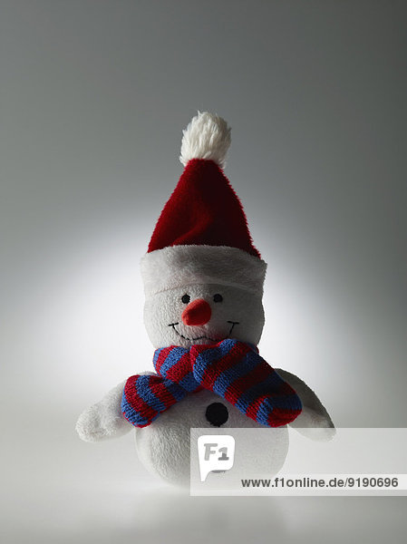 Gefüllter Schneemann mit Schal und Weihnachtsmütze über grauem Hintergrund