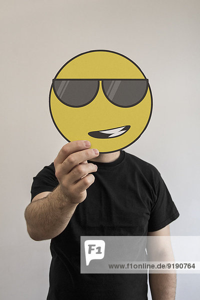 Mann hält eine coole Sonnenbrille mit Emoticon-Gesicht vor seinem Gesicht.