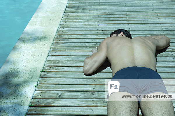 Mann beim Sonnenbaden auf dem Holzdeck neben dem Pool