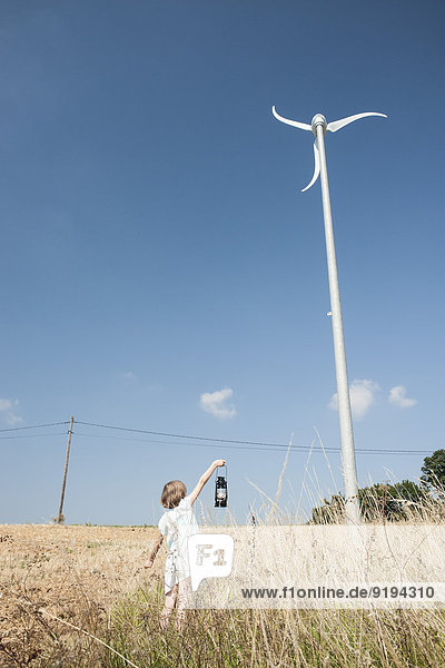 Mädchen steht unter Windkraftanlage  hält Laterne hoch  Stromleitung im Hintergrund