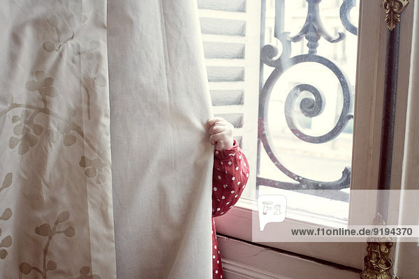 Kind versteckt sich hinter dem Vorhang