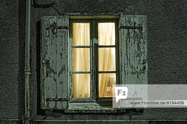 Fenster mit baufälligen nachts beleuchteten Fensterläden