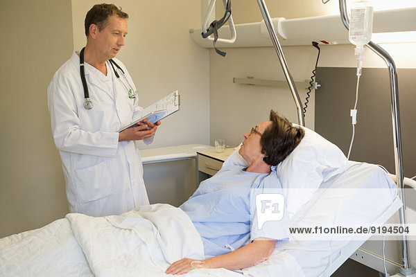 Männlicher Arzt im Gespräch mit dem Patienten auf dem Krankenhausbett