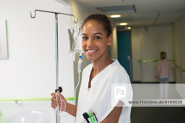 Portrait of a female nurse holding iv drip stand and smiling in hospital
