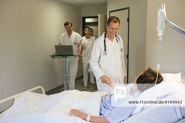 Männlicher Arzt schüttelt dem Patienten die Hand auf dem Krankenhausbett