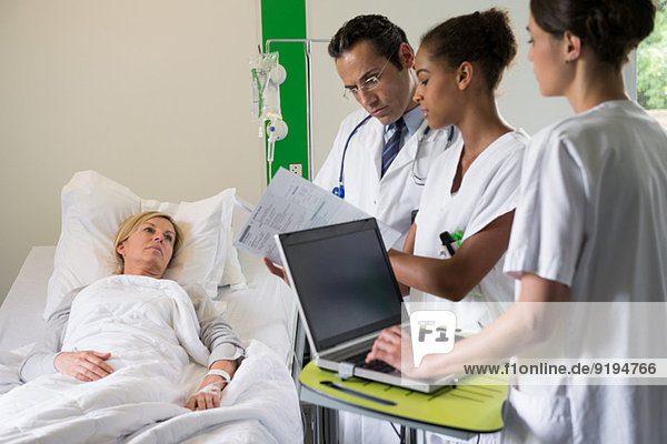 Medical team discussing female patient record on hospital bed