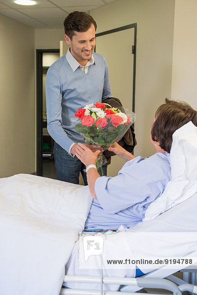 Mann schenkt seiner Mutter einen Blumenstrauß im Krankenhausbett