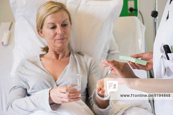 Female nurse giving pill to patient on hospital bed