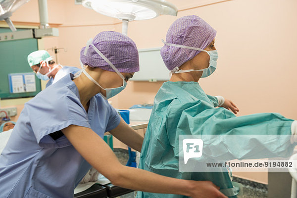 Krankenschwester hilft Chirurgin beim Anziehen der Schutzkleidung